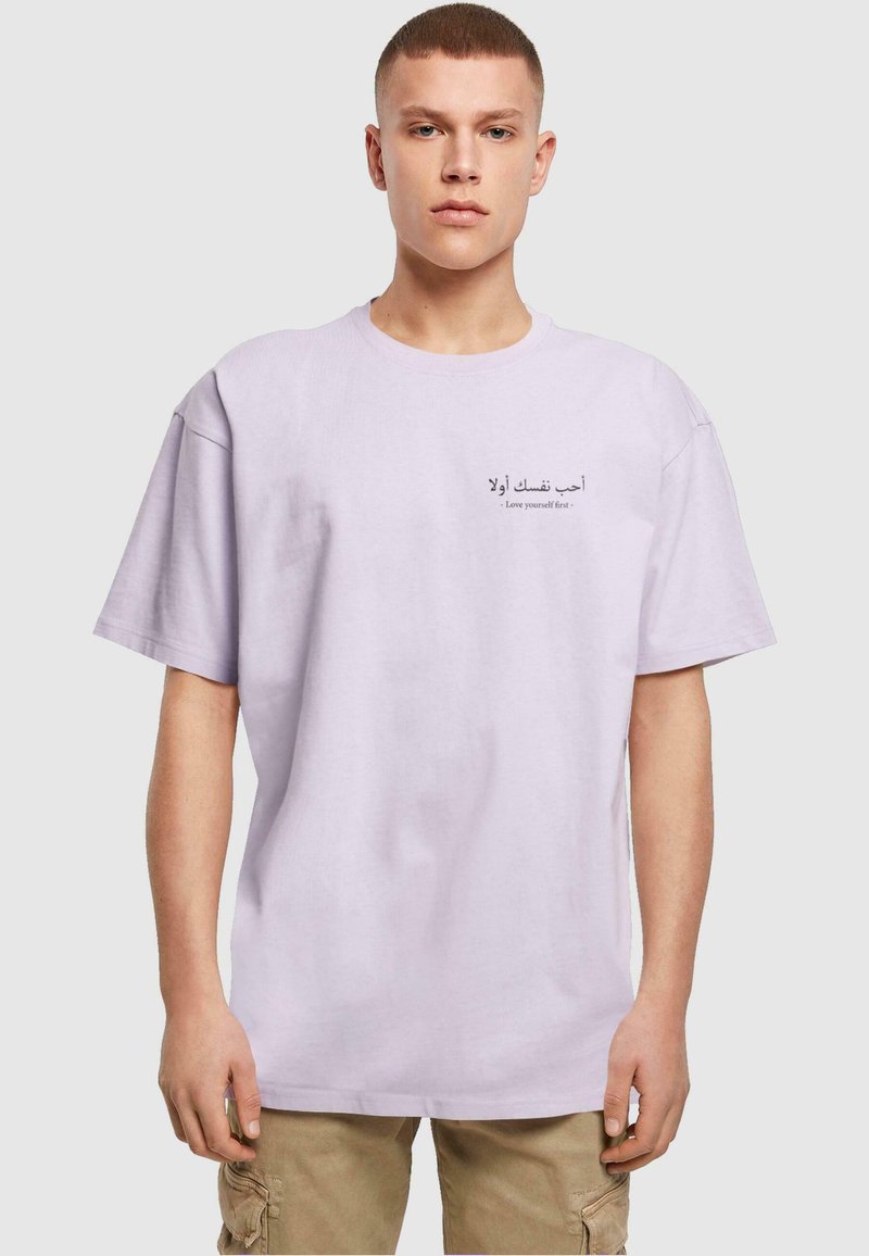 Lyse lilla bomulds t-shirt med rund hals; har trykt arabisk og engelsk tekst på forsiden. Korte ærmer, afslappet pasform.