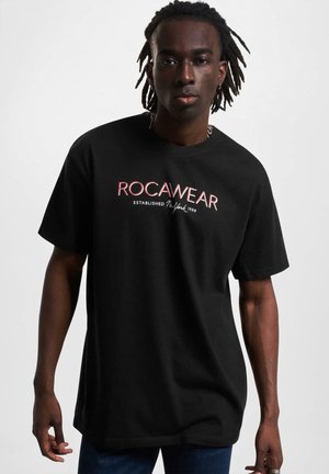 Black short-sleeve t-shirt featuring a white and red "ROCAWEAR" logo and established date, made from soft cotton fabric.