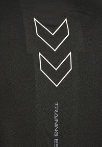 Zwarte trainingskleding met textuurstof. Bevat witte chevronpatronen en de tekst "TRAINING ESSENTIALS", wat een minimalistisch ontwerp benadrukt.