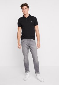 Sort polo skjorte lavet af bomuld, med krave og kortærmer, parret med lysegrå jeans og hvide sneakers. Minimal brandingdetalje.