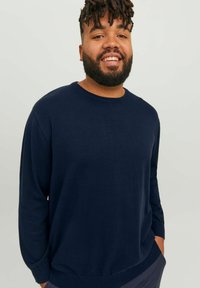 Navy blue pitkähihainein crew neck -neule, joka on valmistettu pehmeästä kankaasta. Siinä on rento istuvuus ja ribbireunat hihoissa ja helmassa.