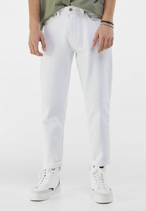 Jeans de mezclilla blanca con un corte recto, que presentan un cierre de botón y puños doblados, combinados con zapatillas blancas. Textura suave, sin patrones.