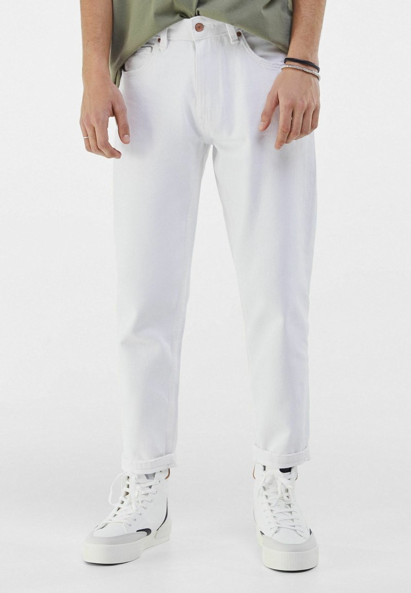 Jeans de mezclilla blanca con un corte recto, que presentan un cierre de botón y puños doblados, combinados con zapatillas blancas. Textura suave, sin patrones.