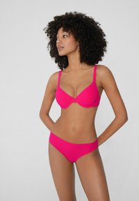 Horkorůžová podprsenka a odpovídající bikinové kalhotky. Podprsenka má tenké ramínka a hladkou texturu, s konturovaným tvarem pro podporu.