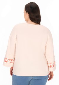 Sweatshirt roz deschis, cu mâneci trei sferturi și manșete cu un model floral, având o croială lejeră. Material moale, cu un gât rotund.