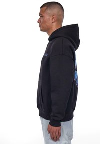 Black hooded sweatshirt with blue logo detail on sleeve, kangaroo pocket, ribbed cuffs, and hem. Fabric appears soft and durable.