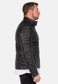 Zwarte leren jas met geborduurde hexagonale patronen, een hoge kraag en met rits gesloten zijzakken, met een getailleerde pasvorm.