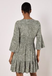 Green paisley-patterned dress with flared sleeves, smocked bodice, and ruffled hem, featuring lightweight fabric and textured design.