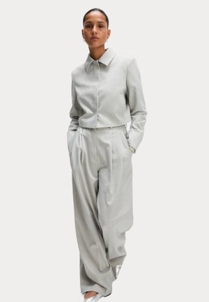 Completo su misura grigio chiaro con giacca corta a bottone e pantaloni palazzo a vita alta. Tessuto liscio con un motivo sottile.