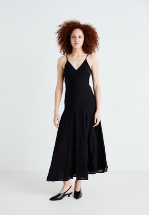 Black spaghetti-strap dress with a V-neck, flowing silhouette, and ankle-length hem. Worn with black pointed-toe slingback shoes.