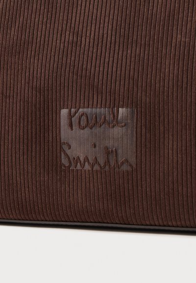 Brūna korduroja audums ar izteiktu ribojumu, uz caurspīdīga plākstera ar izcelta "Paul Smith" logo.