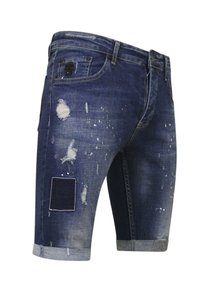 Donkerblauwe denim short met versleten details, verschillende stoffen patches, opgerolde pijpen en een unieke, gestructureerde oppervlakte.