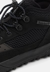 Czarny sneaker Timberland wykonany z siateczki i zamszu, z okrągłymi sznurowadłami, zaokrąglonym noskiem, teksturowaną podeszwą i detalem z logo po boku.