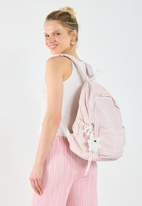 Sac à dos en tissu rayé rose et blanc avec poche avant et porte-clés peluche blanche. Bretelles réglables et forme arrondie.