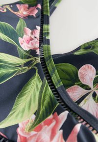 Badpak met een donkere achtergrond met roze bloemenpatronen, groene bladeren en contrasterende zwart-wit stiksels langs de randen.