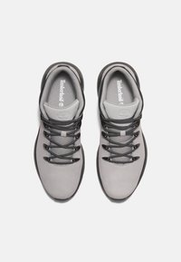 Grå vandringsskor med en slät ovandel, svarta snörningar och en texturerad skör. Har en logotyp på hälkappan och en gummiyttersula.