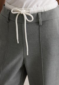 Szare zwężane spodnie z elastycznym pasem, wyposażone w biały ściągacz. Tkanina o gładkiej fakturze z minimalną liczbą szwów.