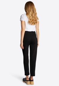 Zwarte broek met hoge taille en gestroomlijnd ontwerp, gemaakt van zachte stof, gecombineerd met een wit T-shirt met korte mouwen en klompen met houten zolen.