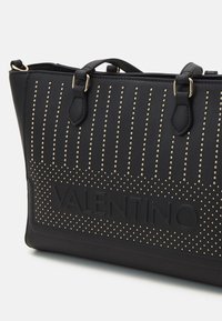 Black tote bag with gold studs, a textured surface, and embossed "VALENTINO" logo. Features dual handles and a structured shape.
