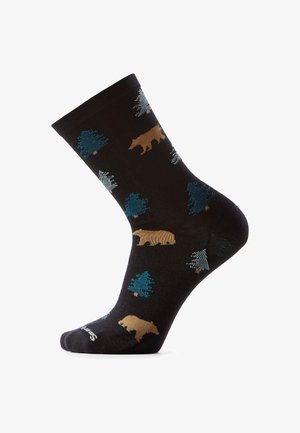 Czarna skarpetka wzorzysta brązowymi niedźwiedziami i niebiesko-zielonymi sosnami, prezentowana na białym tle, z stopą lekko uniesioną do góry.