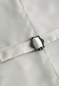 Un tissu gris clair avec une texture lisse présente une boucle décorative en métal noir et une ceinture en satin attachée pour la fermeture.