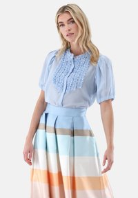 Hellblaue Bluse mit Rüschenfront und kurzen Puffärmeln, kombiniert mit einem mehrfarbig gestreiften Rock in sanften Pastellfarben und Falten.