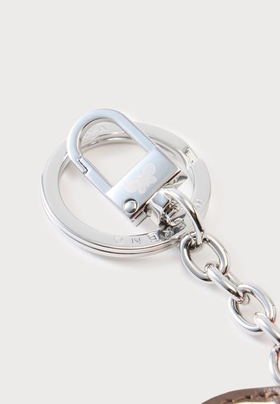 Porte-clés en métal argenté brillant attaché à une chaîne avec un fermoir gravé d’un petit symbole d’abeille sur un fond uni.
