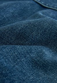 Blå denimtyg med en märkbar twilltextur som visar veck och en slät, något glänsande yta.