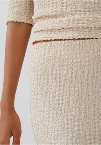 Texturerad, krämfärgad outfit med en samlad design; toppen har korta ärmar och kjolen matchar i textur och färg.