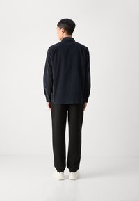 Donkerblauwe corduroy shirt met lange mouwen, rugpas, en knopenmanchetten, gecombineerd met zwarte broek en witte sneakers. Soepele textuur, relaxed fit.