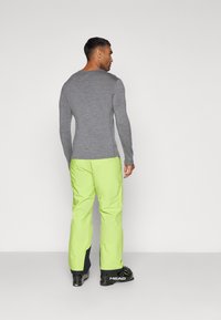 Haut de couche de base à manches longues gris associé à un pantalon de ski vert lime vif. La tenue présente un design ajusté et des bottes de ski noires.