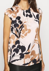 Hellrosa Bluse mit kurzen Cap-Ärmeln, die ein florales Design in Schwarz und Braun aufweist, zarte Falten am Ausschnitt und eine glatte Textur hat.