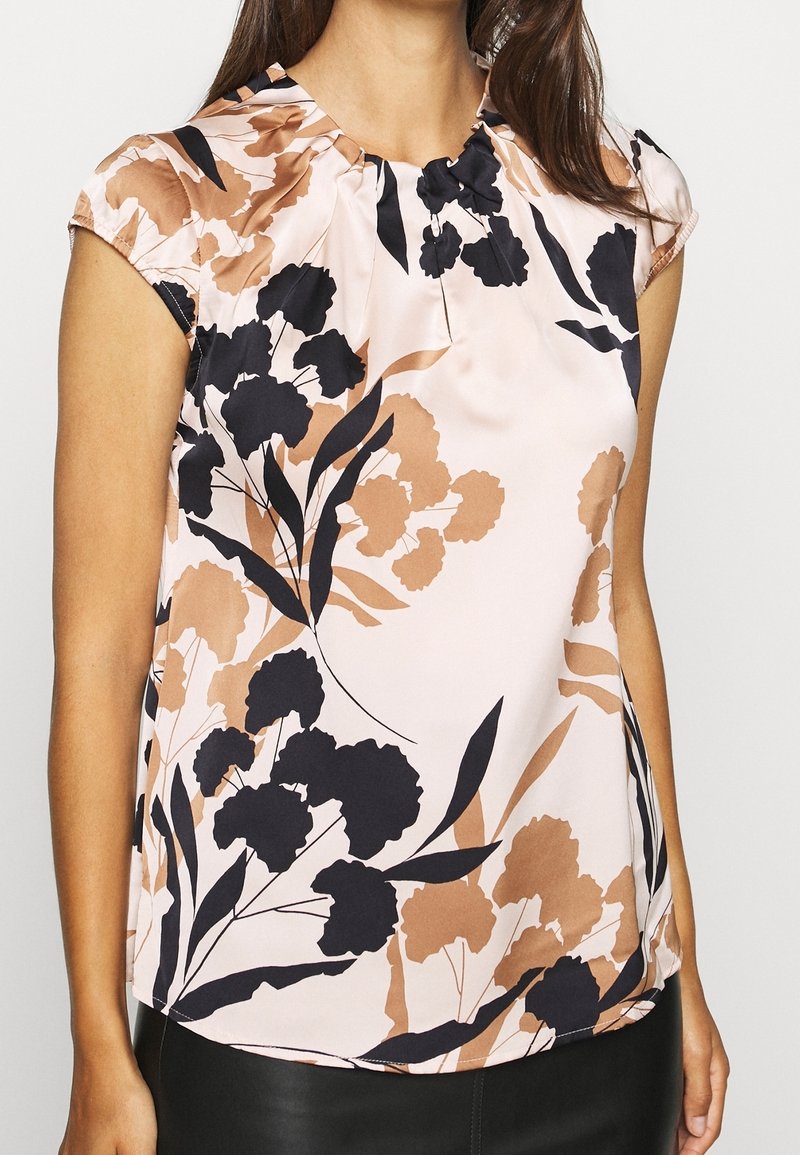 Hellrosa Bluse mit kurzen Cap-Ärmeln, die ein florales Design in Schwarz und Braun aufweist, zarte Falten am Ausschnitt und eine glatte Textur hat.