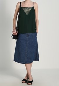 Grön ärmlös topp med spetsdetalj, tillsammans med en knälång denimkjol. Svarta sandaletter och en liten svart väska fullbordar looken.