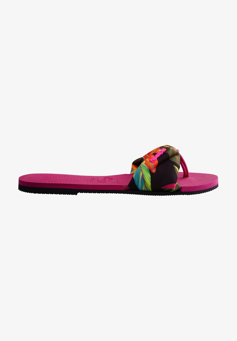 Tongs plates roses avec semelle noire et large bride en tissu ornée d'un motif coloré de feuilles tropicales et de branding rose.