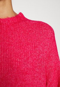 Maglione rosa brillante con una texture a coste, dotato di un collo rotondo e di un tessuto leggero, adatto per l'abbigliamento casual.