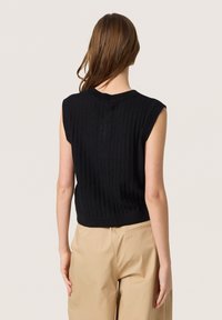 Zwarte geribbelde gebreide mouwloze top met een ronde halslijn, voorzien van een textuurpatroon en een aansluitende zoom, gecombineerd met beige losse broeken.