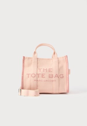 Ružová plátená taška na rameno s dvomi hornými držadlami, na ktorej je potlačený nápis "THE TOTE BAG MARC JACOBS," a nastaviteľným popruhom.