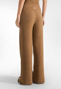 Pantalones de lana anchos y marrones con una textura suave, que cuentan con una cinturilla elástica gruesa. Detalle de costura visible que recorre las piernas.