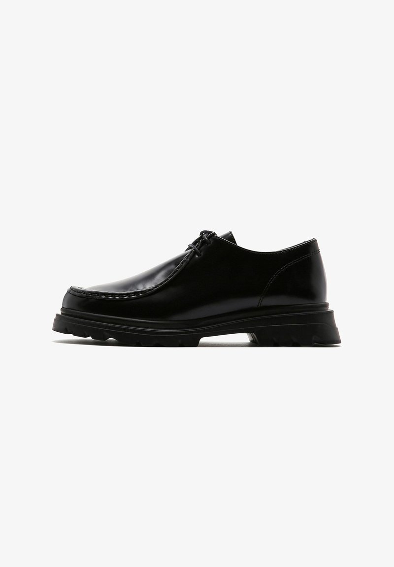 Chaussures en cuir noir au design épuré, avec un bout arrondi et des coutures visibles. Elles possèdent une semelle en caoutchouc noir épais et texturé pour une meilleure adhérence.