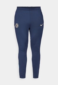 Granatowe spodnie sportowe o dopasowanym kroju, wykonane z gładkiego materiału. Posiadają logo Chelsea FC oraz mały beżowy znak Nike na boku.