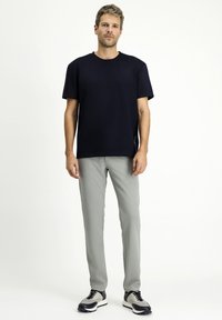 T-shirt blu navy a maniche corte, abbinata a pantaloni slim-fit grigio chiaro e sneakers nero-grigie, in piedi su uno sfondo neutro.