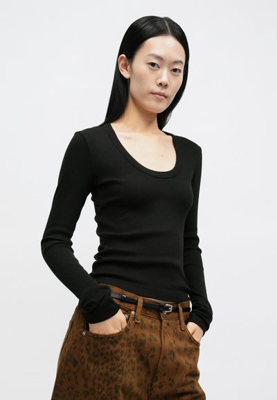 Camisola preta de manga comprida com nervuras e decote redondo, combinada com calças castanhas com padrão de estampa de leopardo.