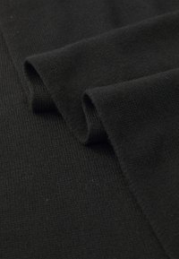 Zwarte gebreide stof met een geribbelde textuur, voorzien van gladde, gevouwen randen. Het materiaal ziet er zacht en warm uit.