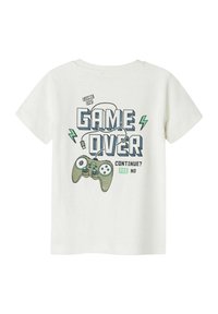 T-shirt bianco in cotone con una grafica che mostra un controller di gioco verde, la scritta "GAME OVER" decorata con accenti di fulmine e "CONTINUE? YES NO".