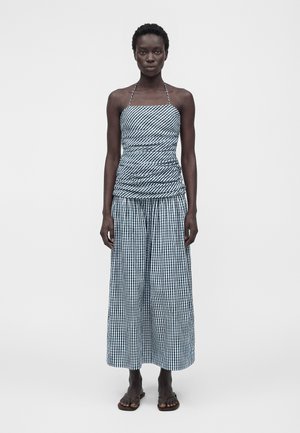 Kvinde står med front mod kamera iført en navy- og hvidternet haltertop og vidde bukser med sorte sandaler på en ensartet hvid baggrund.