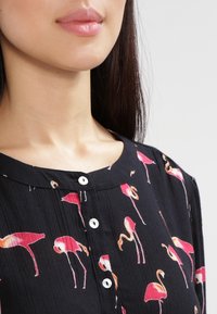 Schwarze Bluse mit einem Muster aus rosa Flamingos, mit einem runden Ausschnitt und Knopfdetails an der Vorderseite. Strukturierter Stoff.