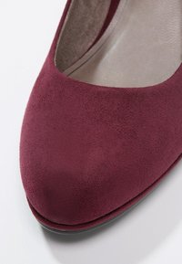 Gros plan d’une chaussure femme en daim bordeaux avec bout rond et doublure intérieure beige matelassée.