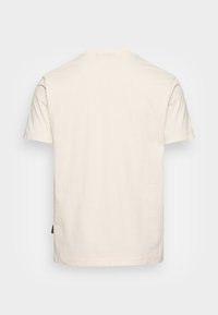 Camiseta de algodón crema, de manga corta, cuello redondo, diseño simple, corte recto. Presenta una pequeña etiqueta de la marca en el dobladillo.