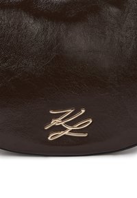 Sac en cuir brun avec une surface texturée et un accent logo doré. Présente une forme arrondie et une finition brillante.